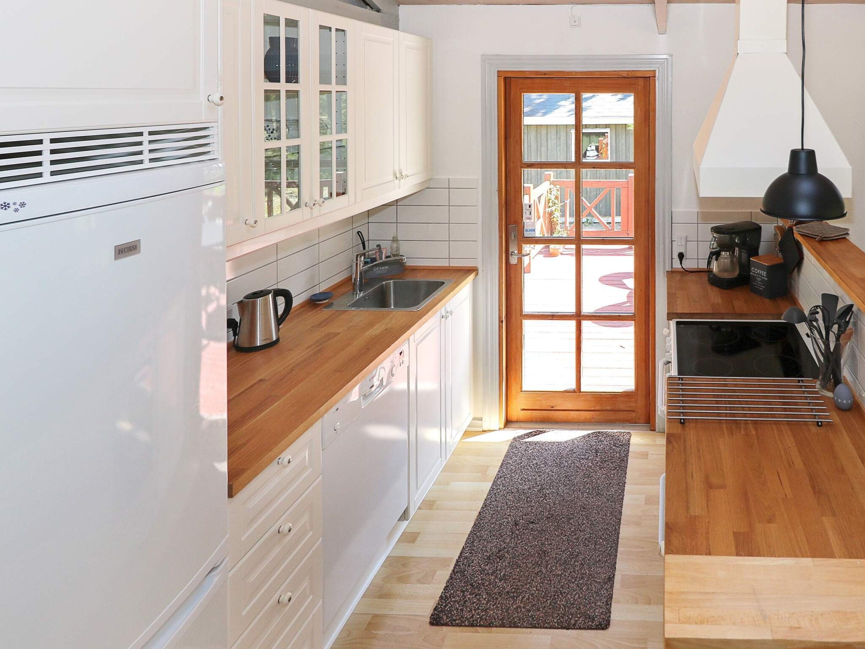 A kitchen with white cabinets, a wooden countertop, a coffee maker, and a black pendant light.