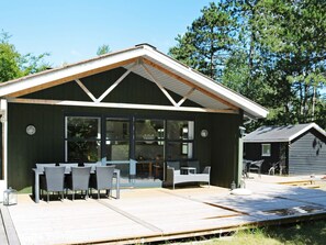 Uma cabana moderna com um alpendre amplo, mobiliário de exterior e uma pequena construção adjacente.