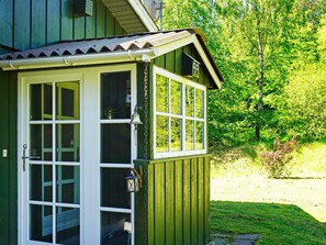 A green wooden structure with a white door and windows, surrounded by greenery.