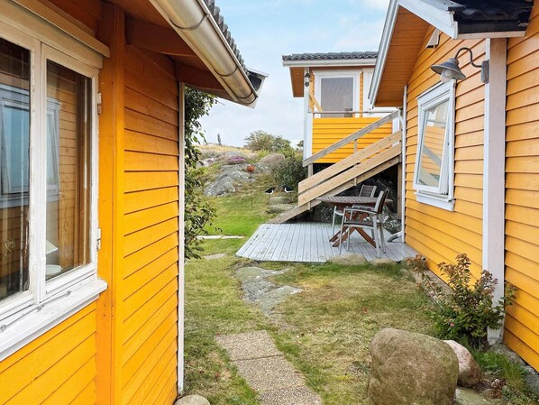 A yellow wooden house with a wooden deck, a small outdoor table, and a staircase leading to a second level. - 3 Person Holiday Home in Ockero (Öckerö)