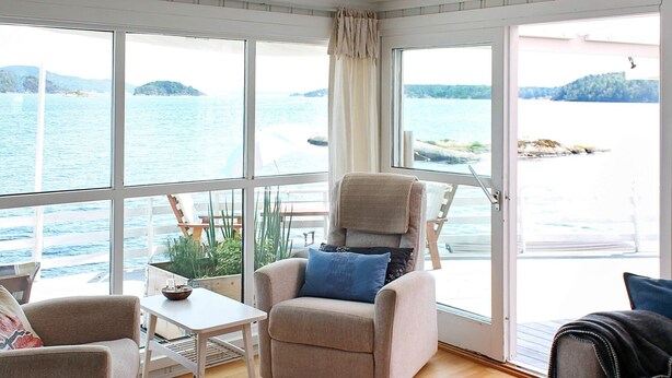 A cozy room with a large window overlooking a body of water, a cushioned chair, a small table, and a view of a dock and boats. - 6 Person Holiday Home in Brevik (Porsgrunn)