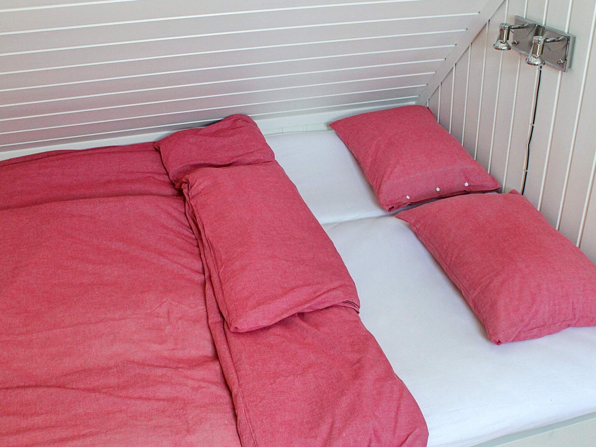 A single-bed room with a white mattress and red bedding.