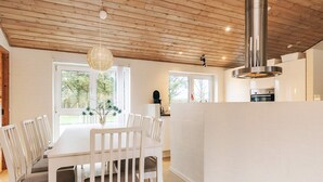 A modern kitchen with white cabinetry, a stainless steel range hood, and a dining area with a white table and chairs. - 5 Star Holiday Home in Hjorring (Hjørring)