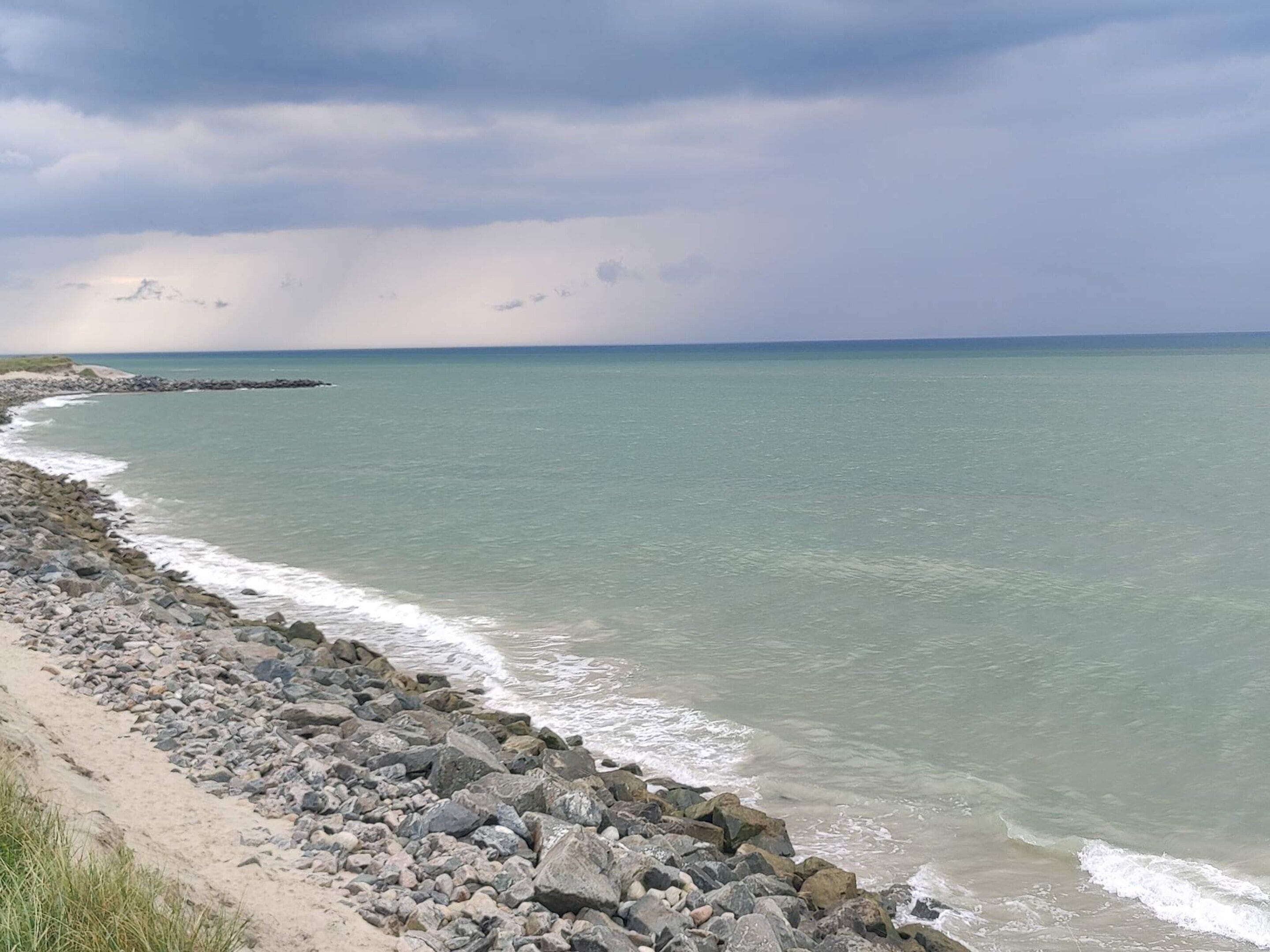 A coastal landscape with a rocky shoreline and calm sea under a cloudy sky.