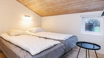 Et soveværelse med to senge, et lille rundt bord og et vindue.