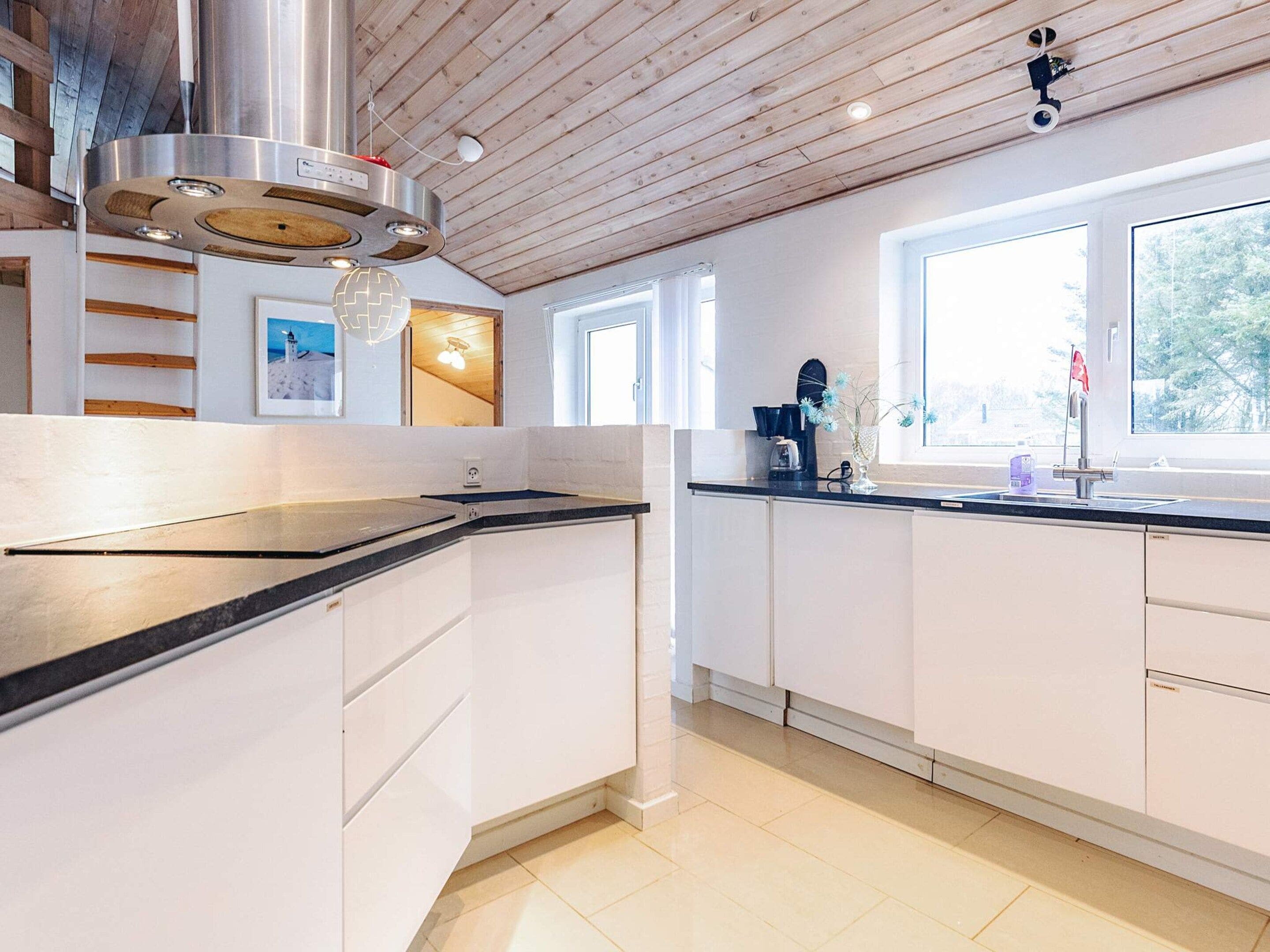 A modern kitchen with white cabinets, a stainless steel range hood, and a window providing natural light.
