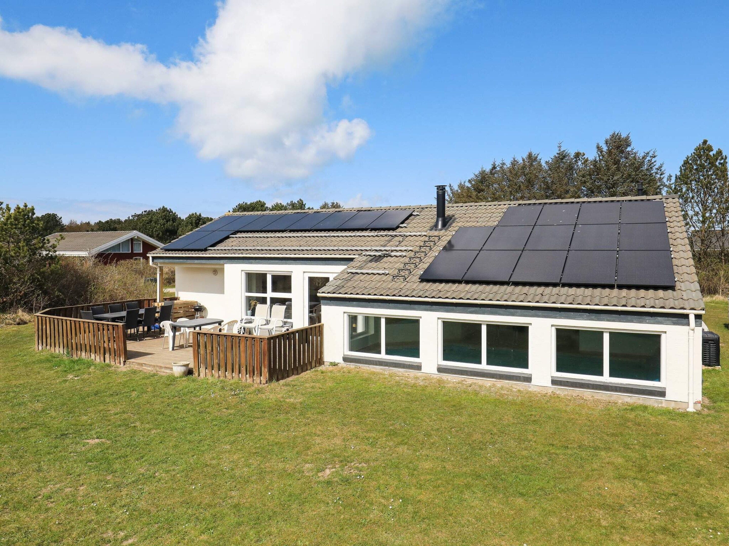 A house with solar panels on the roof, a deck with outdoor furniture, and a large windowed front.