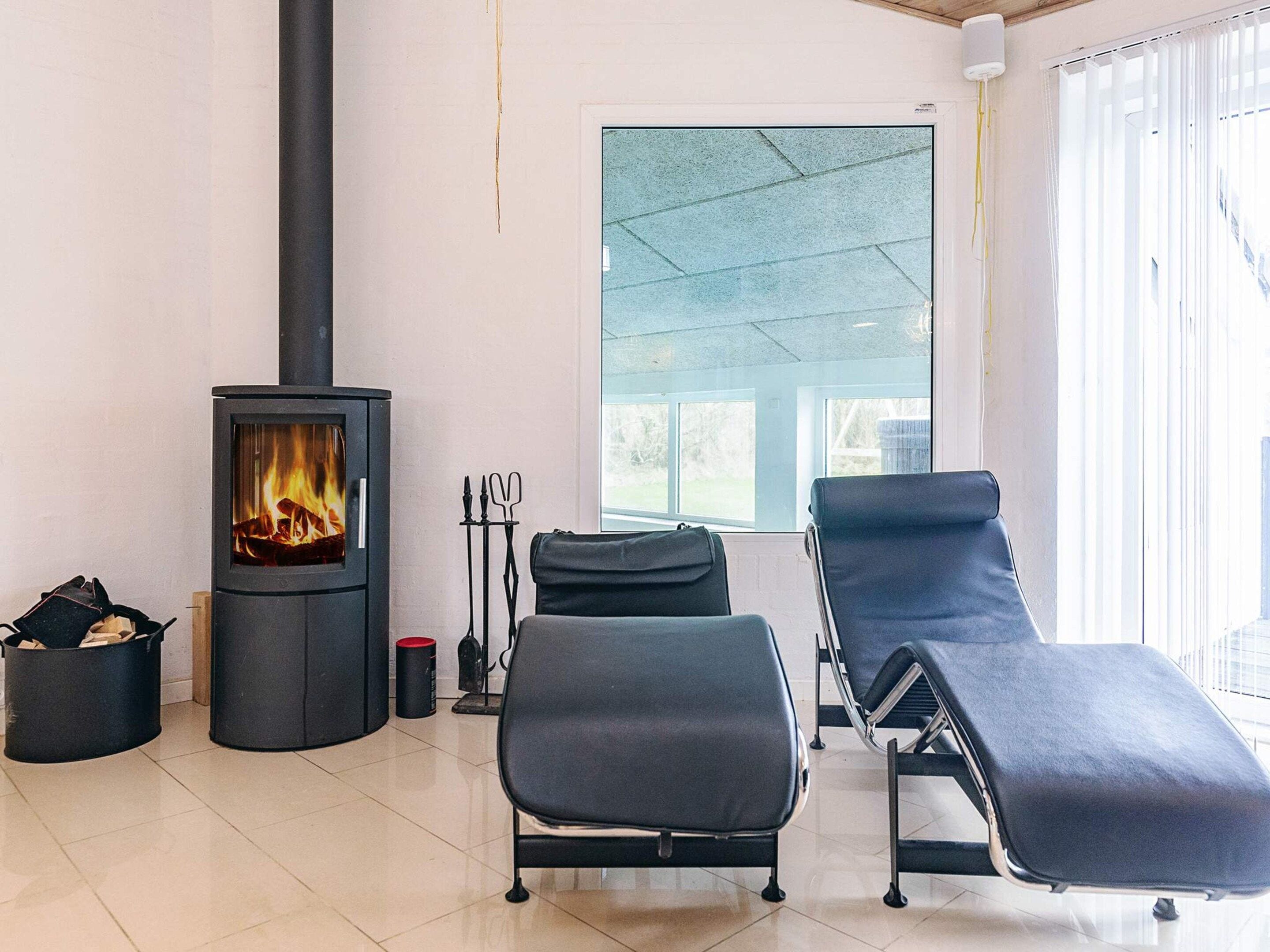 A modern living room with a wood-burning stove, two lounge chairs, and a large window.