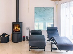A modern living room with a wood-burning stove, two lounge chairs, and a large window. - 5 Star Holiday Home in Hjorring (Hjørring)