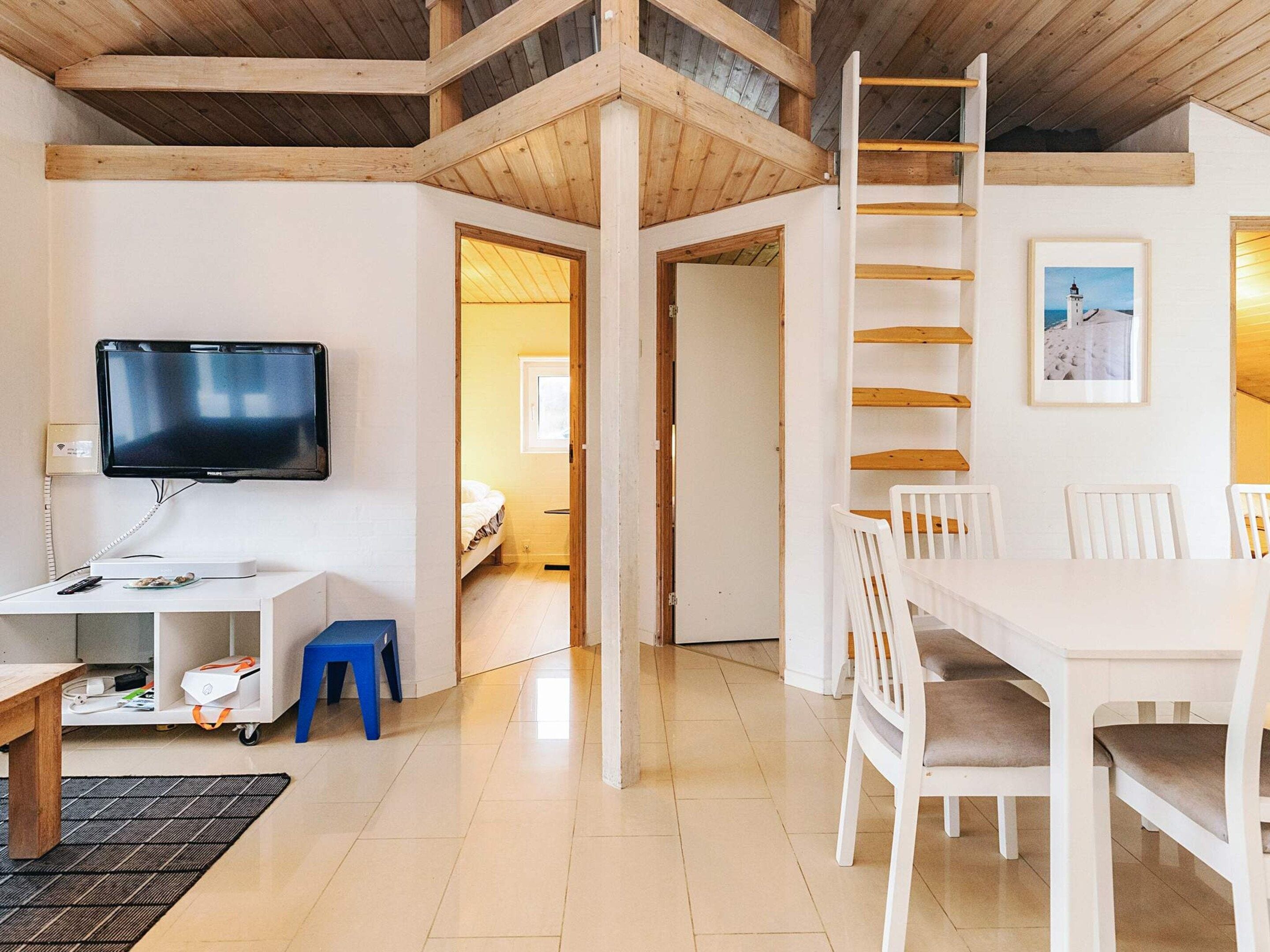 A room with a TV, a desk, a chair, a dining table, and a ladder.