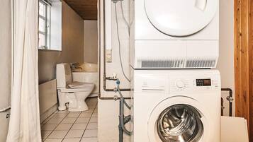 Et lille badeværelse med toilet, vaskemaskine og bruseforhæng.