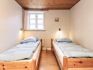 Een kamer met twee houten bedden, een raam met gordijnen, een aan de muur hangend schilderij en een bedlampje.
