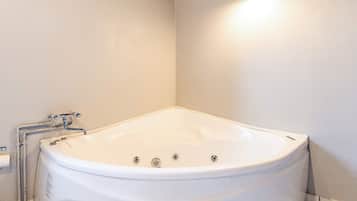 A white bathtub with a wooden ceiling and a wall-mounted light fixture.