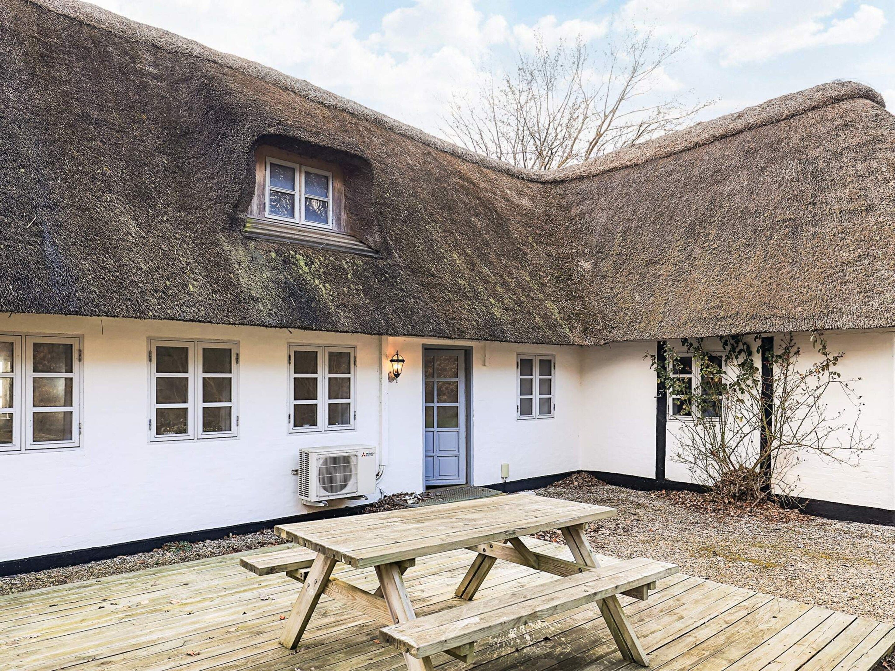 A thatched-roof cottage with a wooden deck and a single air conditioning unit.