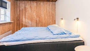 A bedroom with a wooden slatted ceiling, a bed with blue bedding, a bedside table, and two wall-mounted lights.