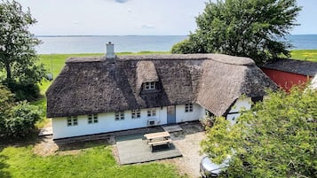 A traditional thatched-roof house with a wooden deck and a view of the sea.