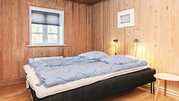 A single bed with a black frame and a blue quilt in a room with wooden walls and a sloped ceiling.