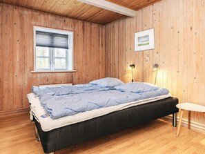 Un lit simple avec un cadre noir et une couette bleue, dans une pièce aux murs en bois et au plafond en pente.