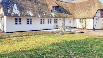 A thatched-roof house with a white exterior, a wooden deck, and a small garden area.