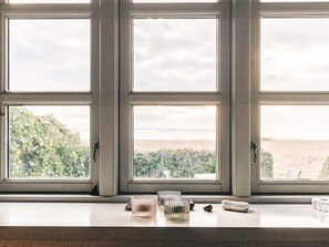 A window with three panes, a wooden sill, and a view of greenery and a distant landscape. - 8 Person Holiday Home in Svendborg (Svendborg)