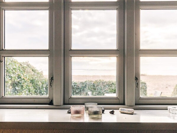 Une fenêtre à trois carreaux, un rebord en bois et une vue sur la verdure et un paysage lointain.