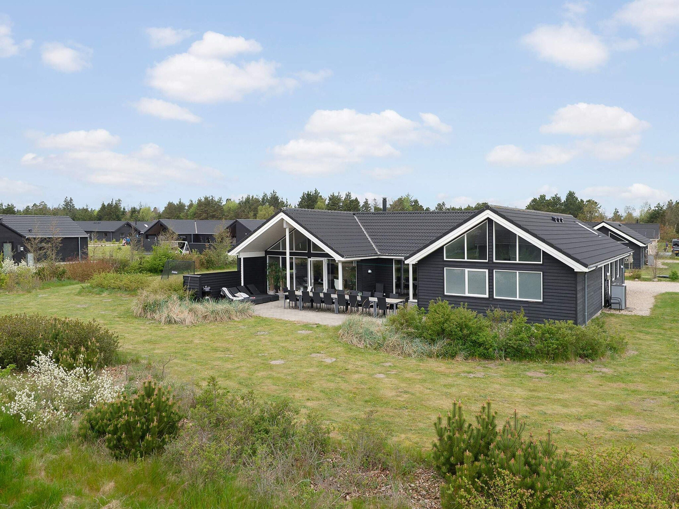 Et moderne hus med terrasse, omgivet af græs og andre lignende huse.