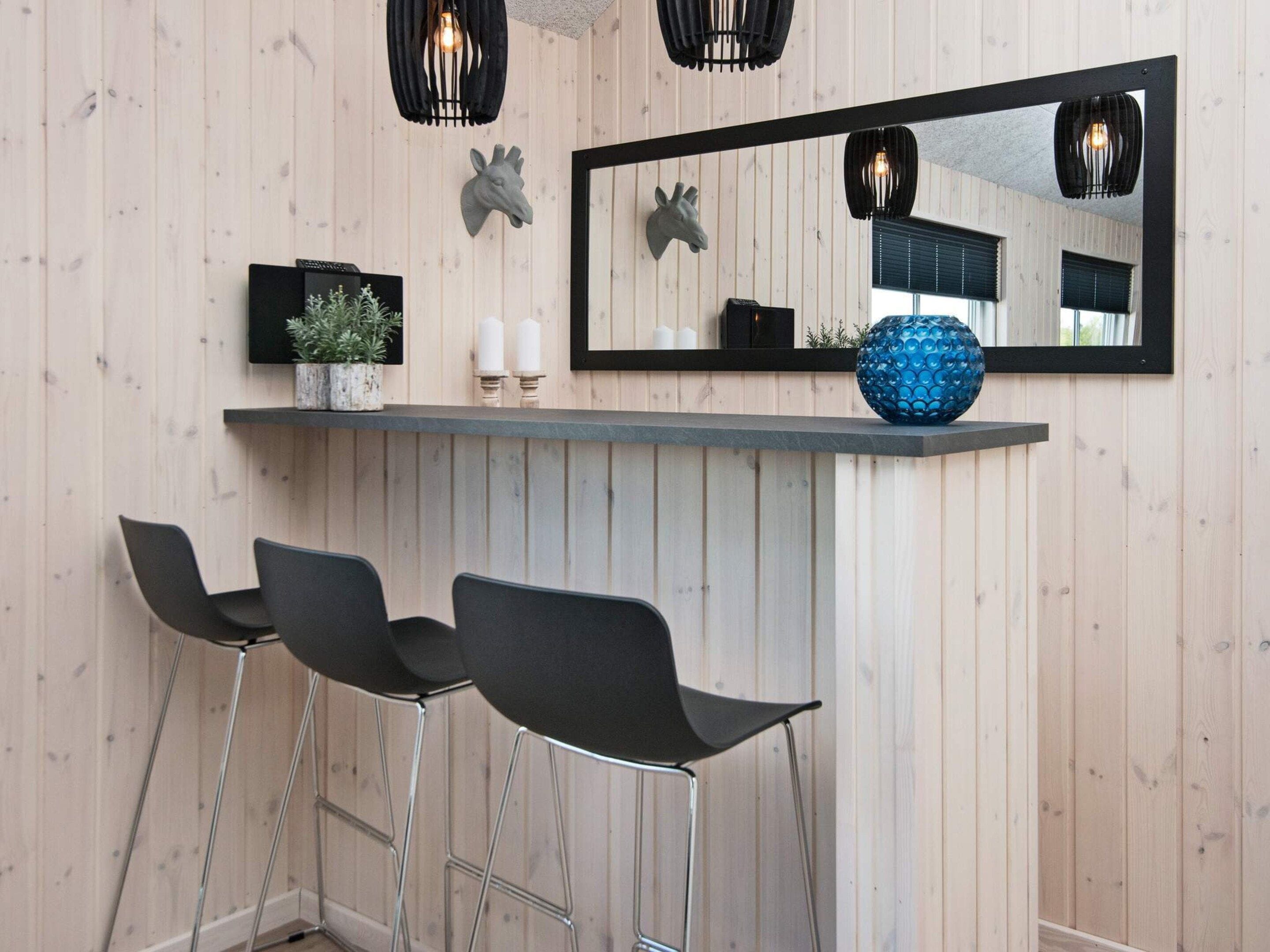 A bar area with a mirror, two candles, a blue vase, and three black bar stools.