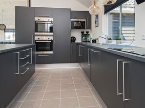A modern kitchen with grey cabinetry, stainless steel appliances, and a large island with a sink. - 5 Star Holiday Home in Norre Nebel (Norre Nebel)