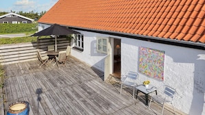 Um deck de madeira com mesa e cadeiras, um guarda-sol preto e um vaso decorativo.