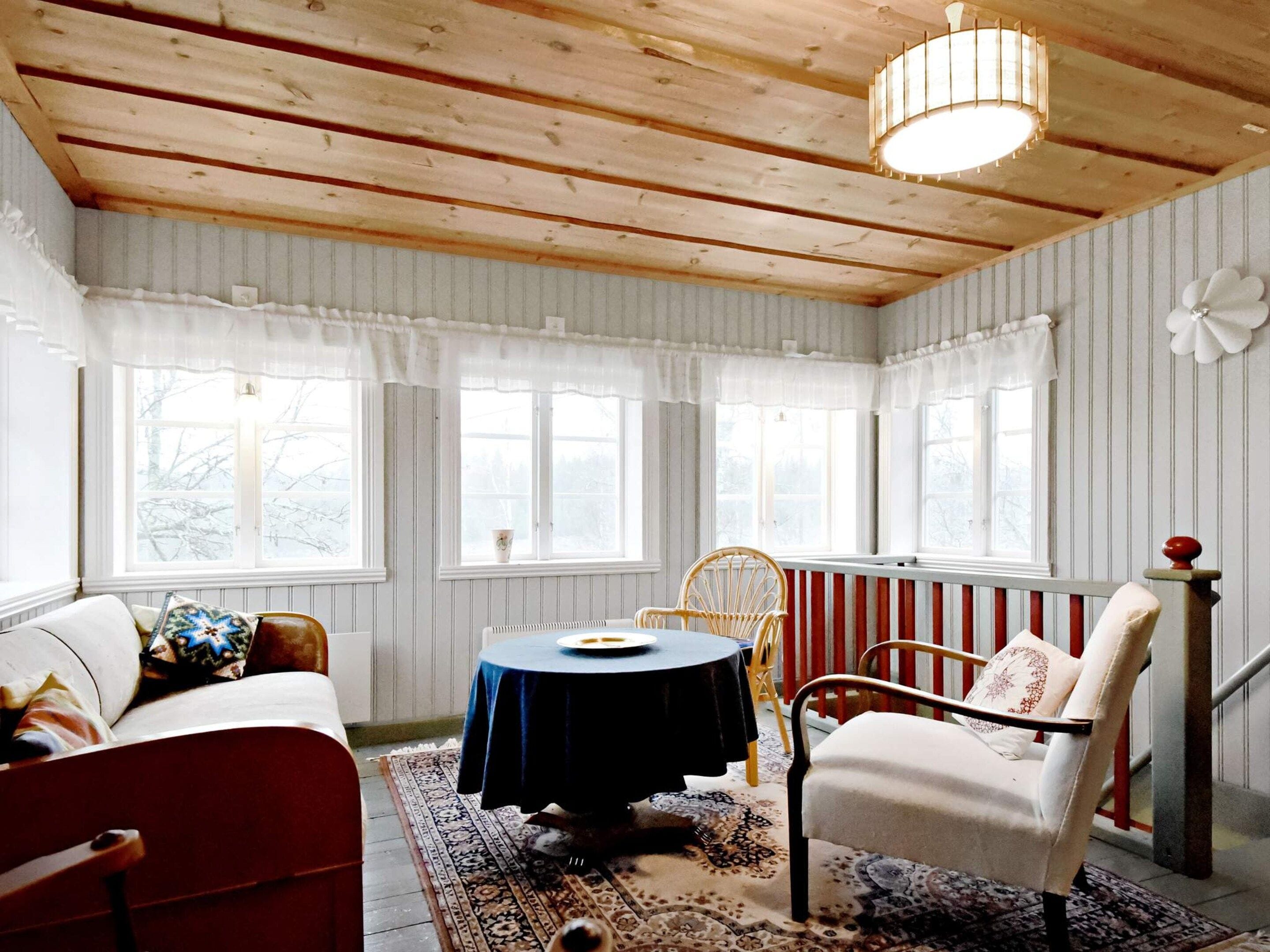 A cozy room with a wooden ceiling, a round table, a sofa, and a chair.