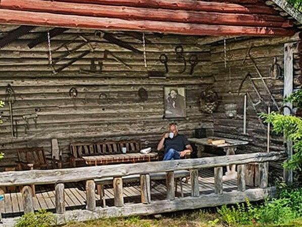 A rustic log cabin with a porch, wooden furniture, and a small table. - 8 Person Holiday Home in Ostmark (Östmark)