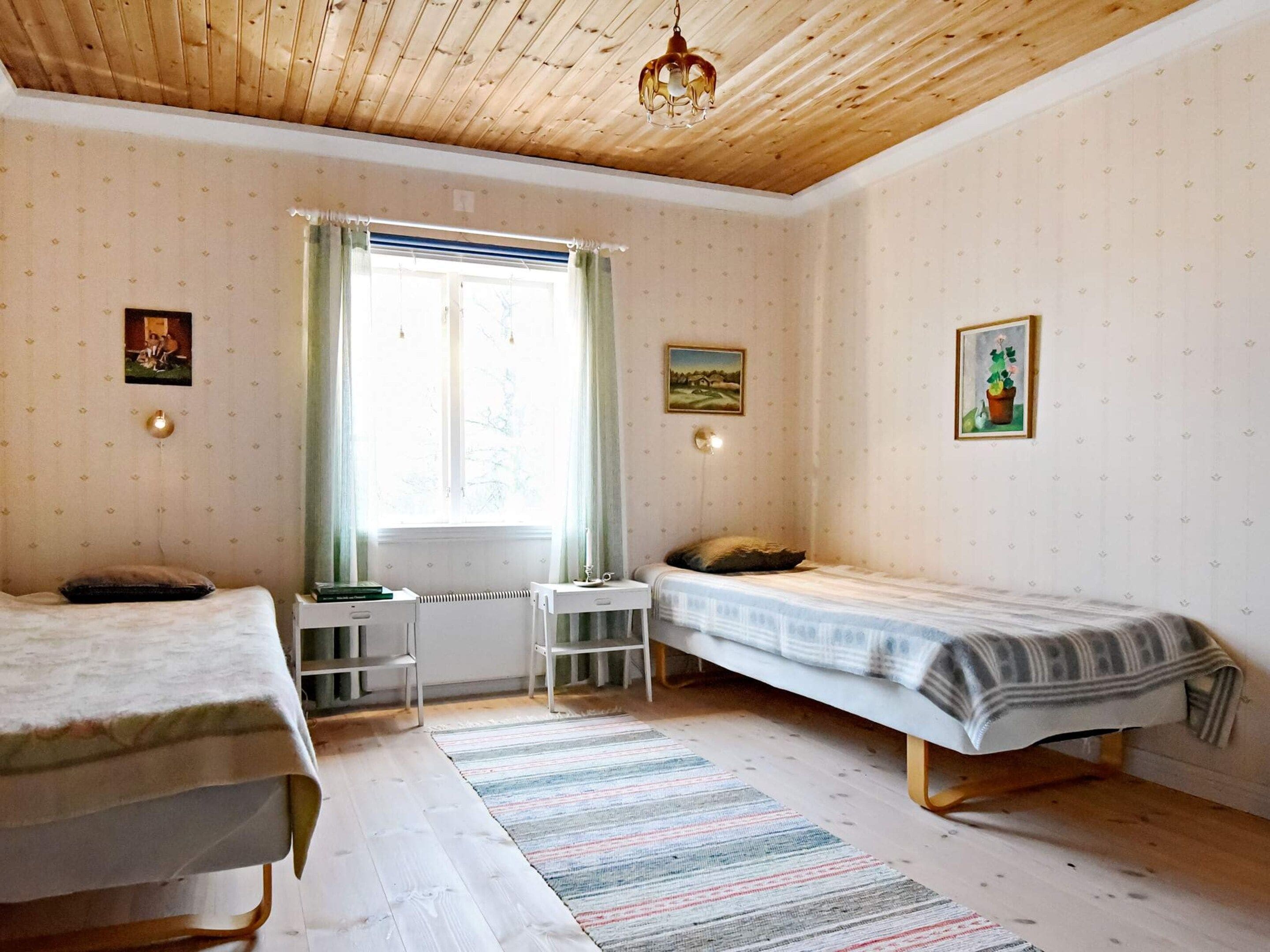 A room with two single beds, a radiator, a window with curtains, and a ceiling light fixture.