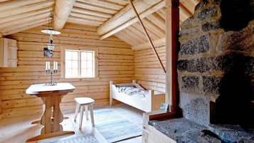 A log cabin interior with a stone fireplace, a bed, a table with candles, and a window.