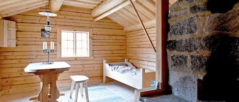 L’intérieur d’une cabane en rondins, avec une cheminée en pierre, un lit, une table avec des bougies et une fenêtre.