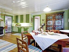 A dining area with a table set for four, chairs, a patterned rug, and a kitchen in the background.