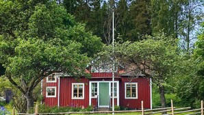 A red wooden house with a green door, surrounded by a wooden fence and trees. - 6 Person Holiday Home in Ullared (Ullared)