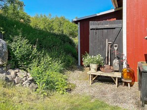 A rustic outdoor area with a red wooden shed, a wooden bench, a potted plant, and gardening tools. - 6 Person Holiday Home in Ullared (Ullared)