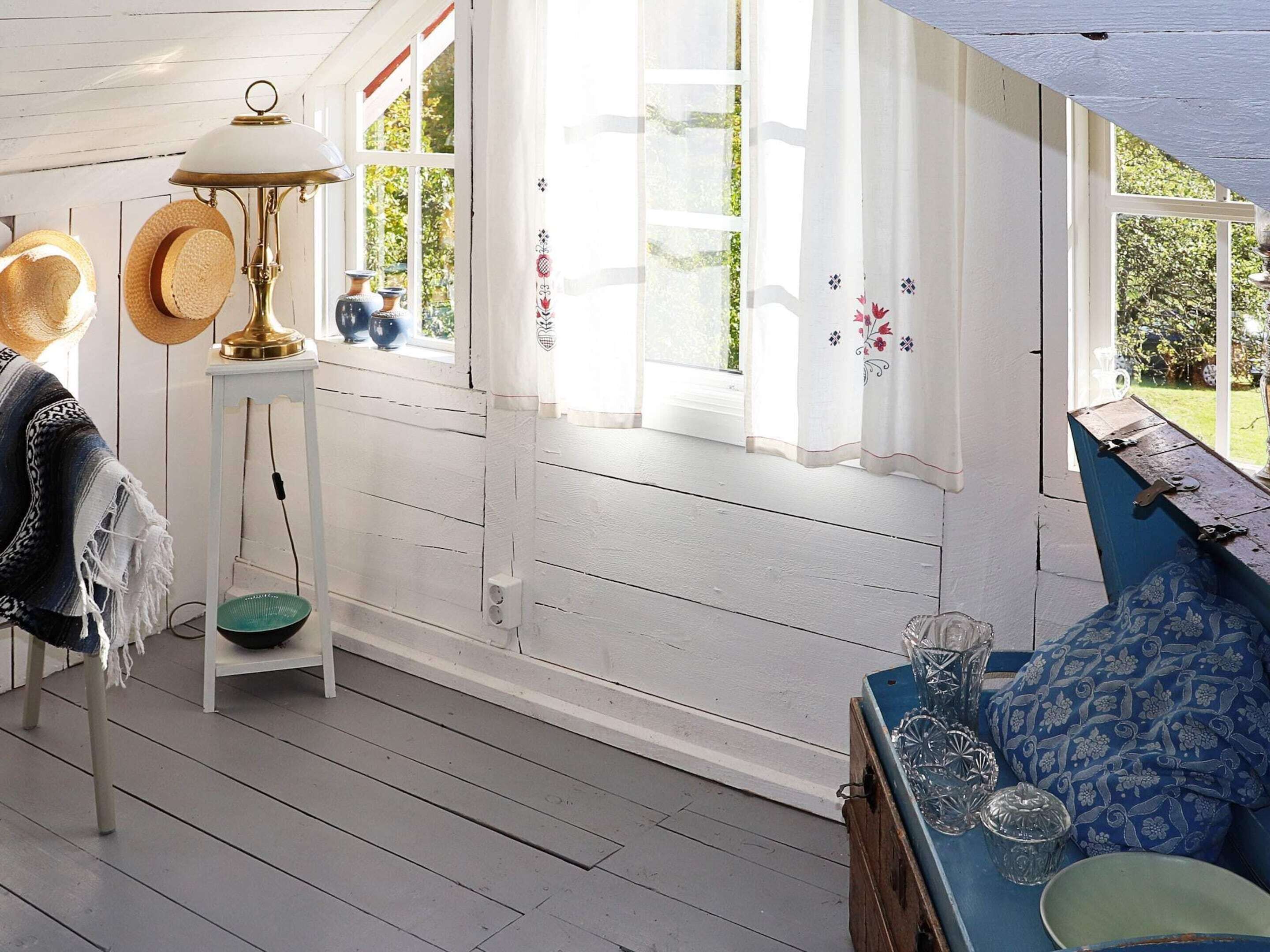 Una habitación acogedora con piso de madera, un sofá azul, una mesita con adornos y una ventana con cortinas.