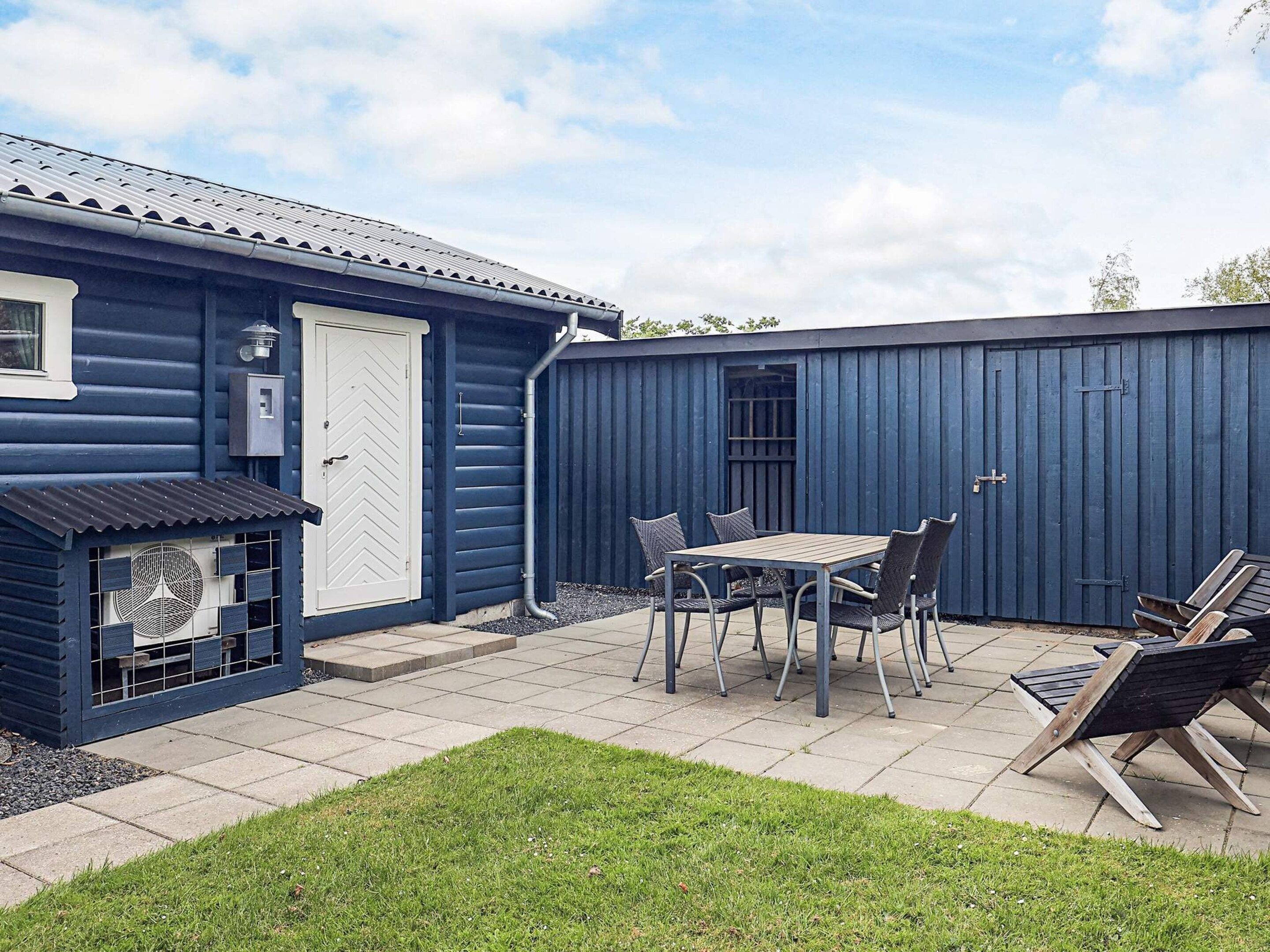 A blue building with a patio area, a table with chairs, and a grill.