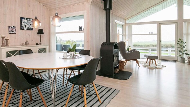 Een ruime kamer met een grote eettafel, moderne stoelen, een open haard en grote ramen met uitzicht.