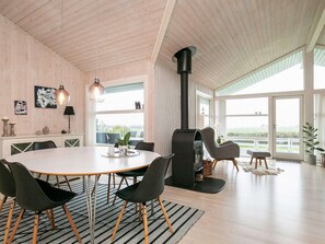 A spacious room with a large dining table, modern chairs, a fireplace, and large windows offering a view. - 4 Star Holiday Home in Svendborg (Svendborg)