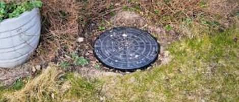 A manhole cover in a grassy area with a white planter nearby.