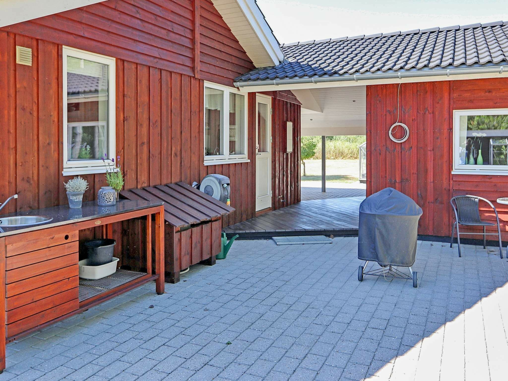 Ein Holzhaus mit einer Terrasse, die einen Grill, Sitzgelegenheiten im Freien und einen kleinen Tisch mit Spüle bietet.