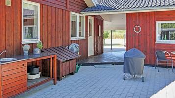 Ein Holzhaus mit einer Terrasse, die einen Grill, Sitzgelegenheiten im Freien und einen kleinen Tisch mit Spüle bietet.