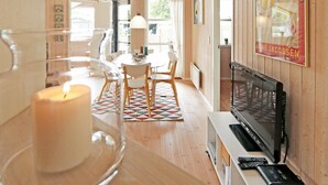 A cozy room with a wooden interior, a dining area with a table and chairs, a TV on a stand, and a large window.