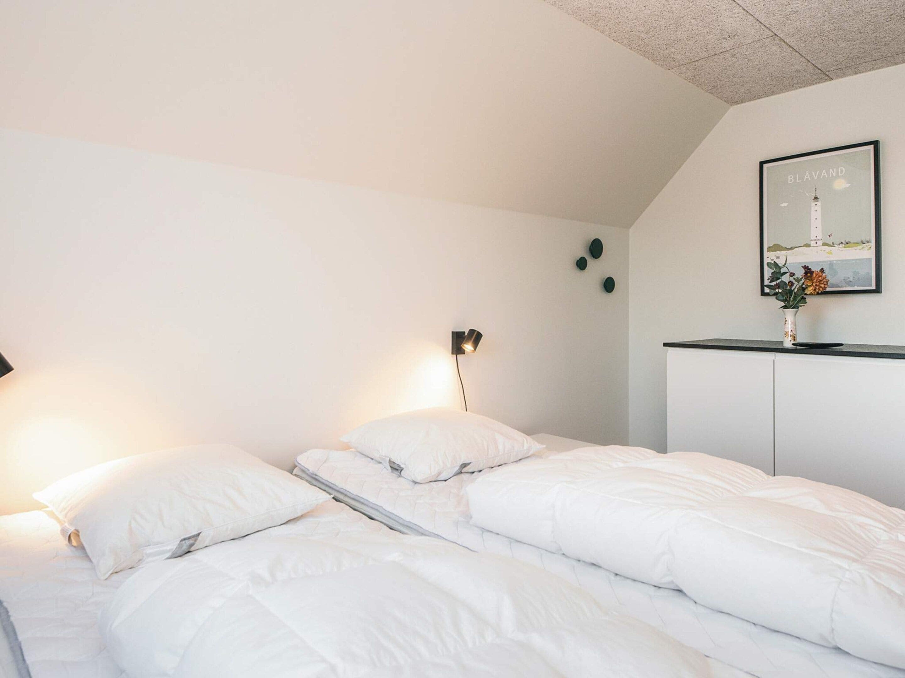 A bedroom with two beds, a nightstand, a lamp, a framed picture on the wall, and a small plant.
