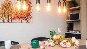 Un coin repas avec une table en bois, des tasses blanches, un vase vert et un arrangement floral.
