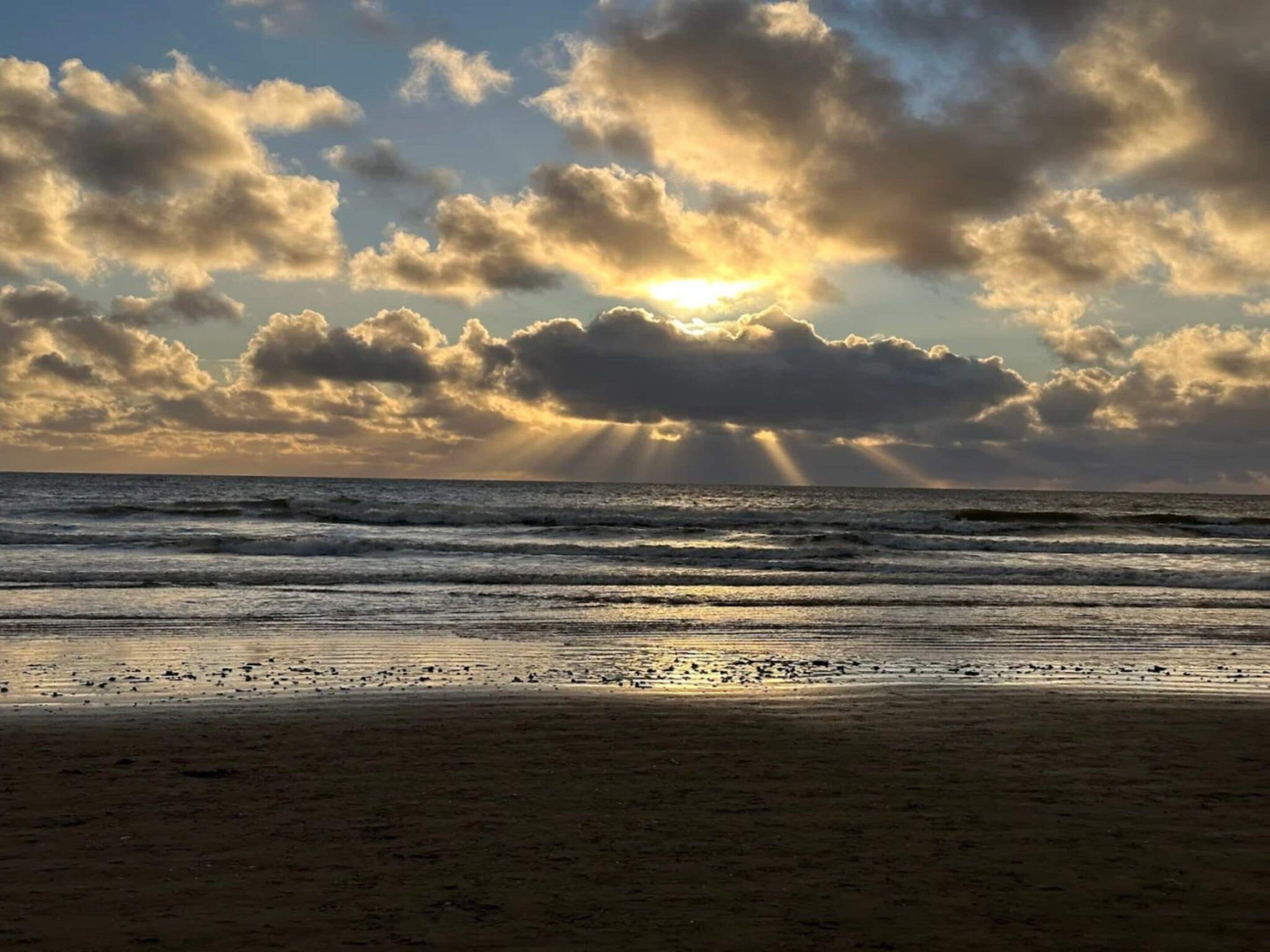 A beach with waves and a cloudy sky with sunlight.