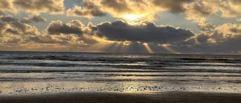 A beach with waves and a cloudy sky with sunlight.