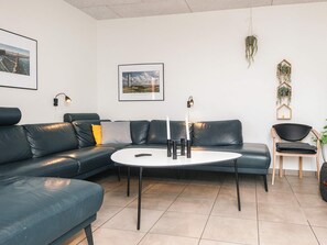 Un salon moderne avec un canapé d’angle, une table basse ronde et deux lampes fixées au mur.